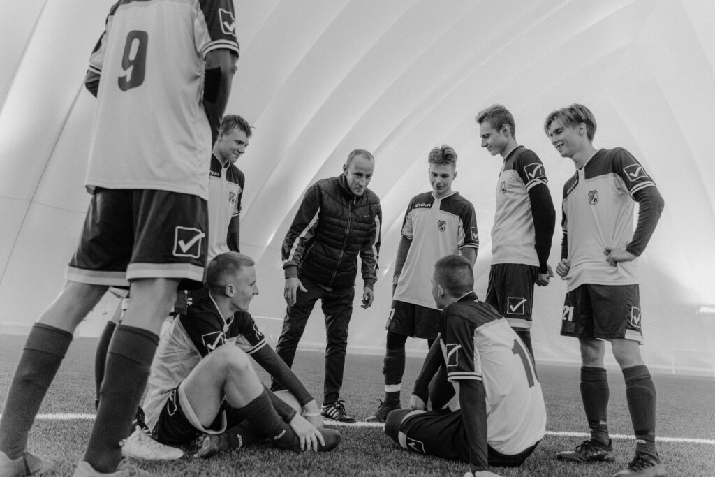 Black and white photo of soccer team and coach planning strategy indoors.